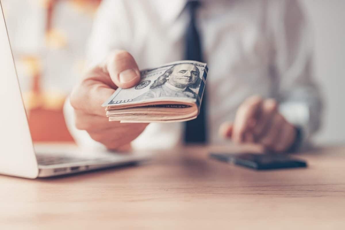 Man dressed professionally handing handful of cash over a table.