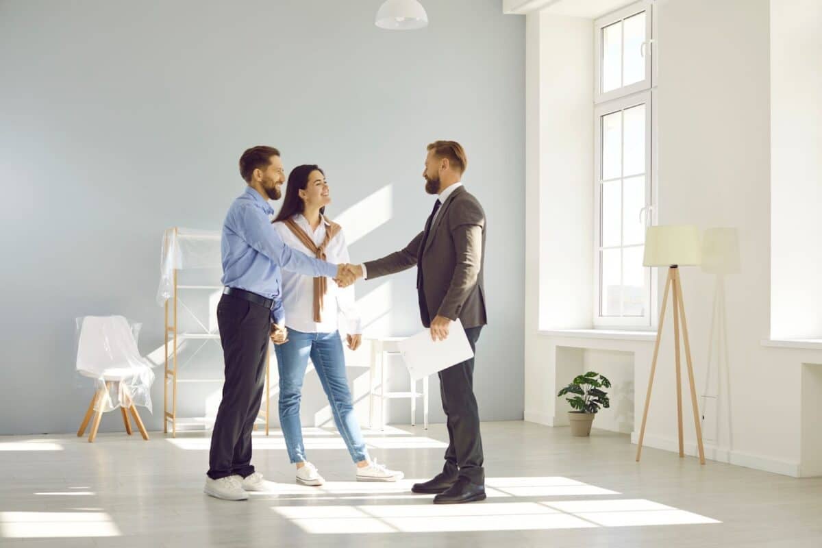 Happy man and woman standing in modern light spacious light living room and shaking hands with real estate agent.