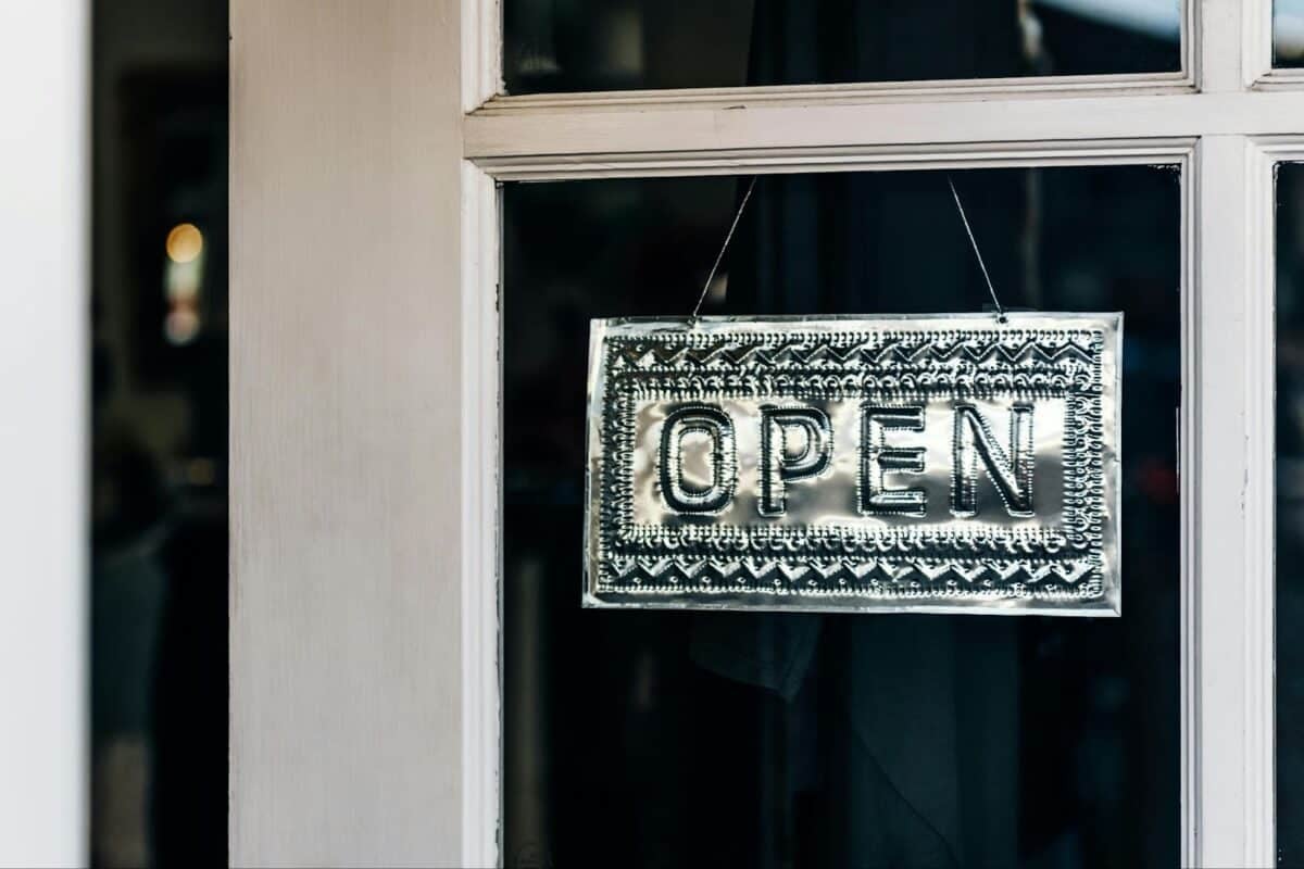 silver open sign hanging on a window of door to a small business.