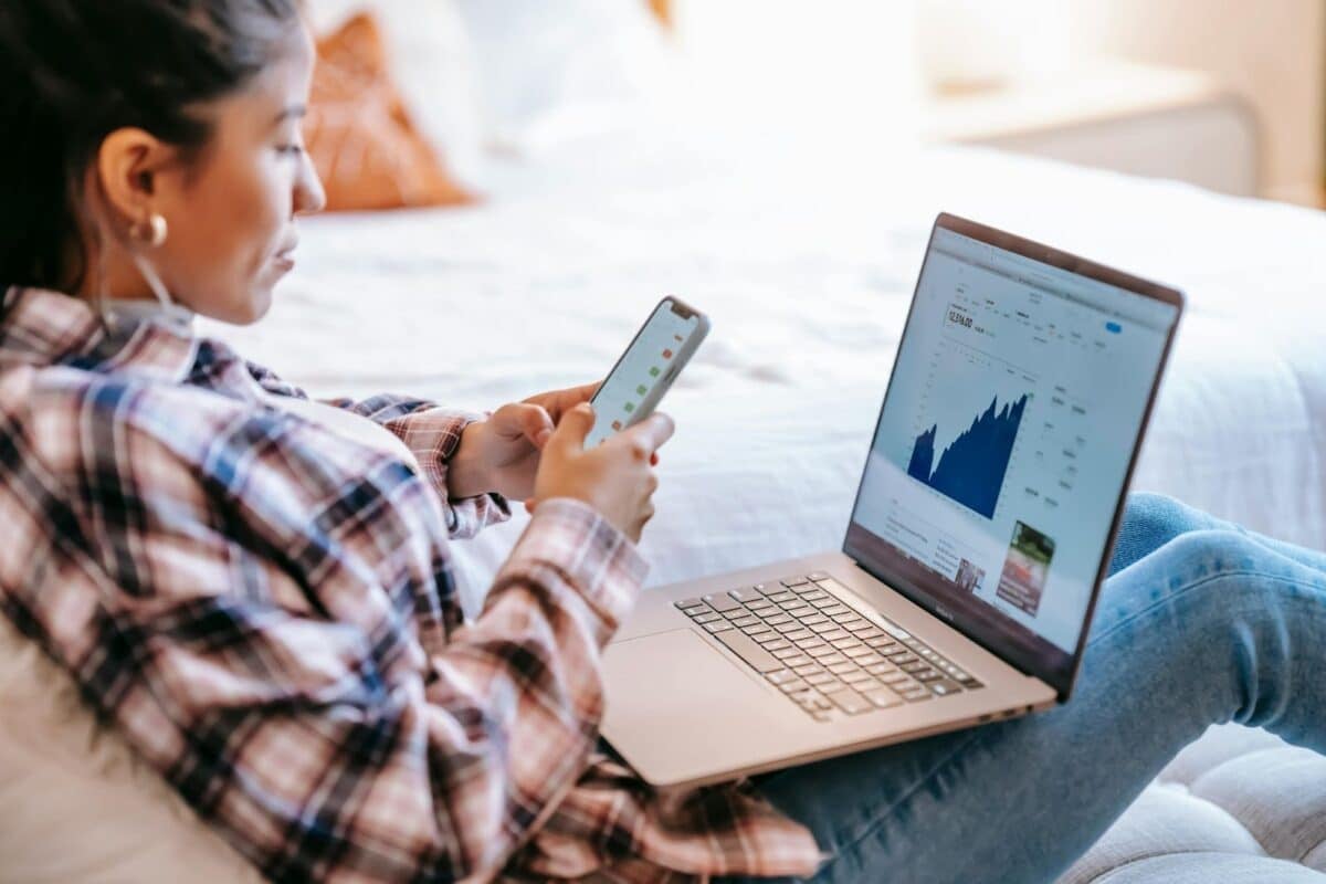 woman at computer holding a sell phone looking at a graph.