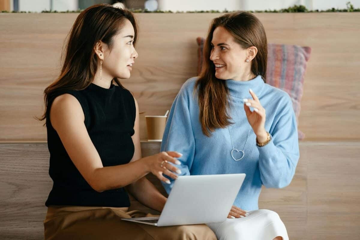 two woman sitting at a coffee shop looking at each other having a conversation.