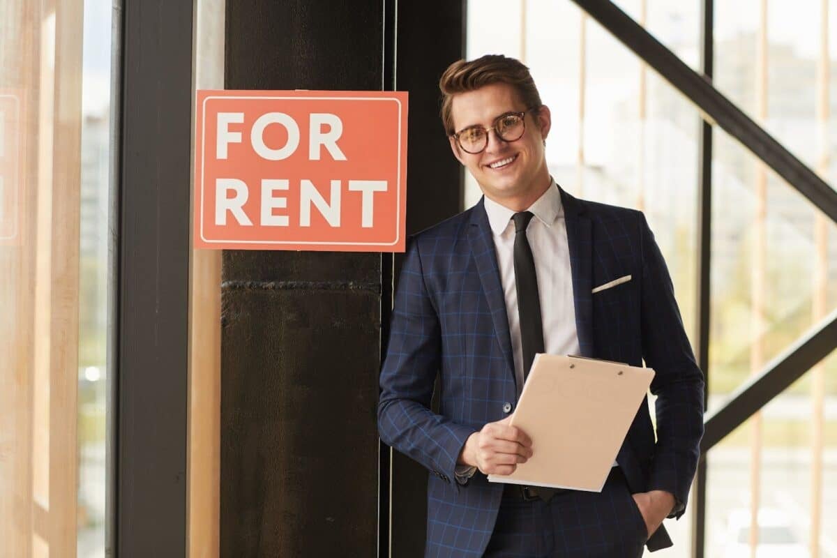 Portrait of a property manager next to a red 'for rent' sign