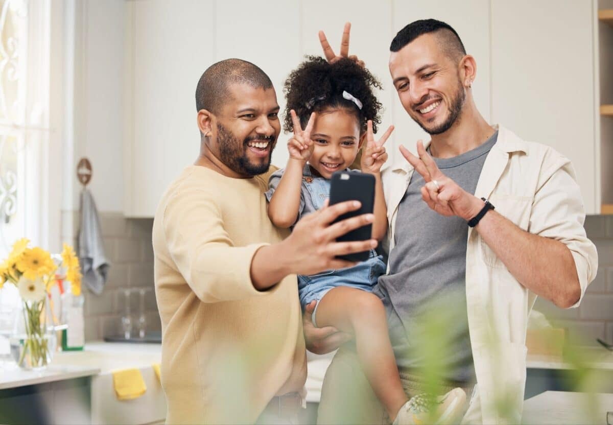 A girl with her gay parents posing for a photo in their kitchen