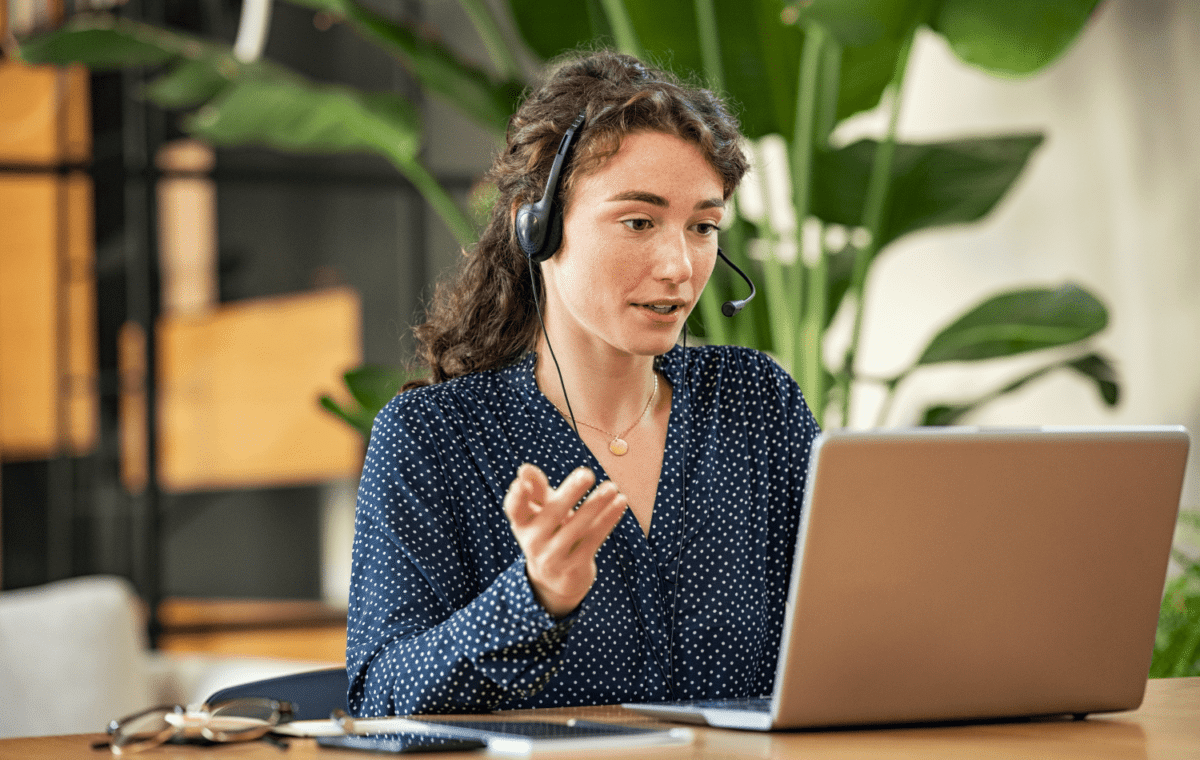 A woman looking at her laptop with a headset on her head, talking on the phone.