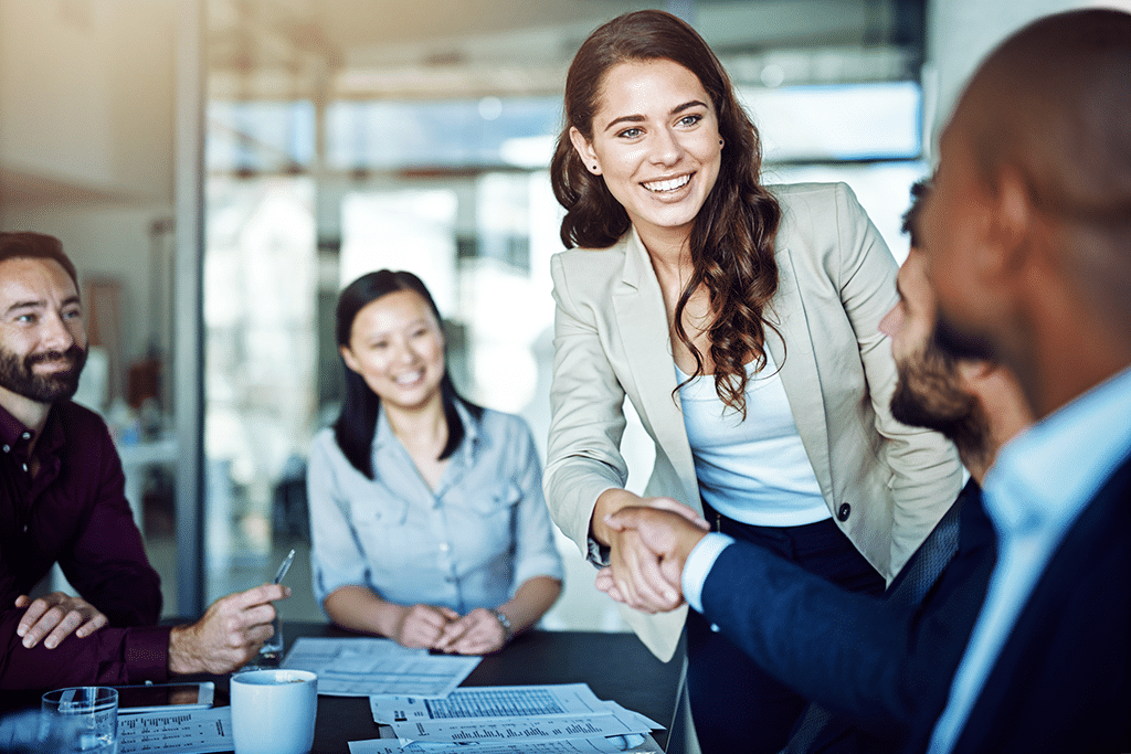 Professional woman confidently shakes hands around a conference table.