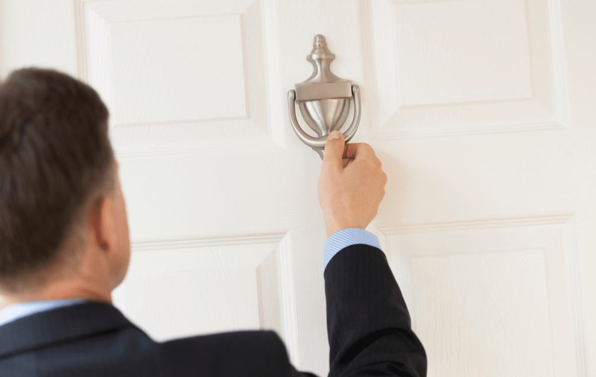 Man in suit knocking an exterior door knocker