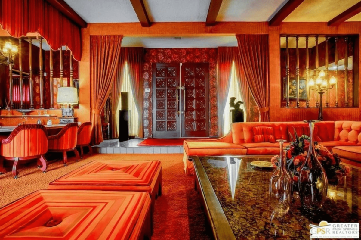 A living room full of orange decor: orange curtains, chairs, carpet, flowers