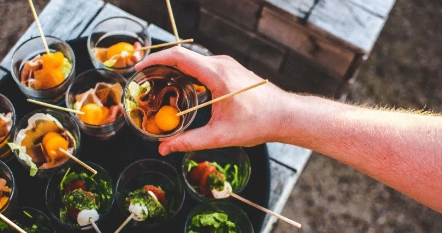 Someone picking up an individual serving of veggies, cheese, and meat in a cup. 