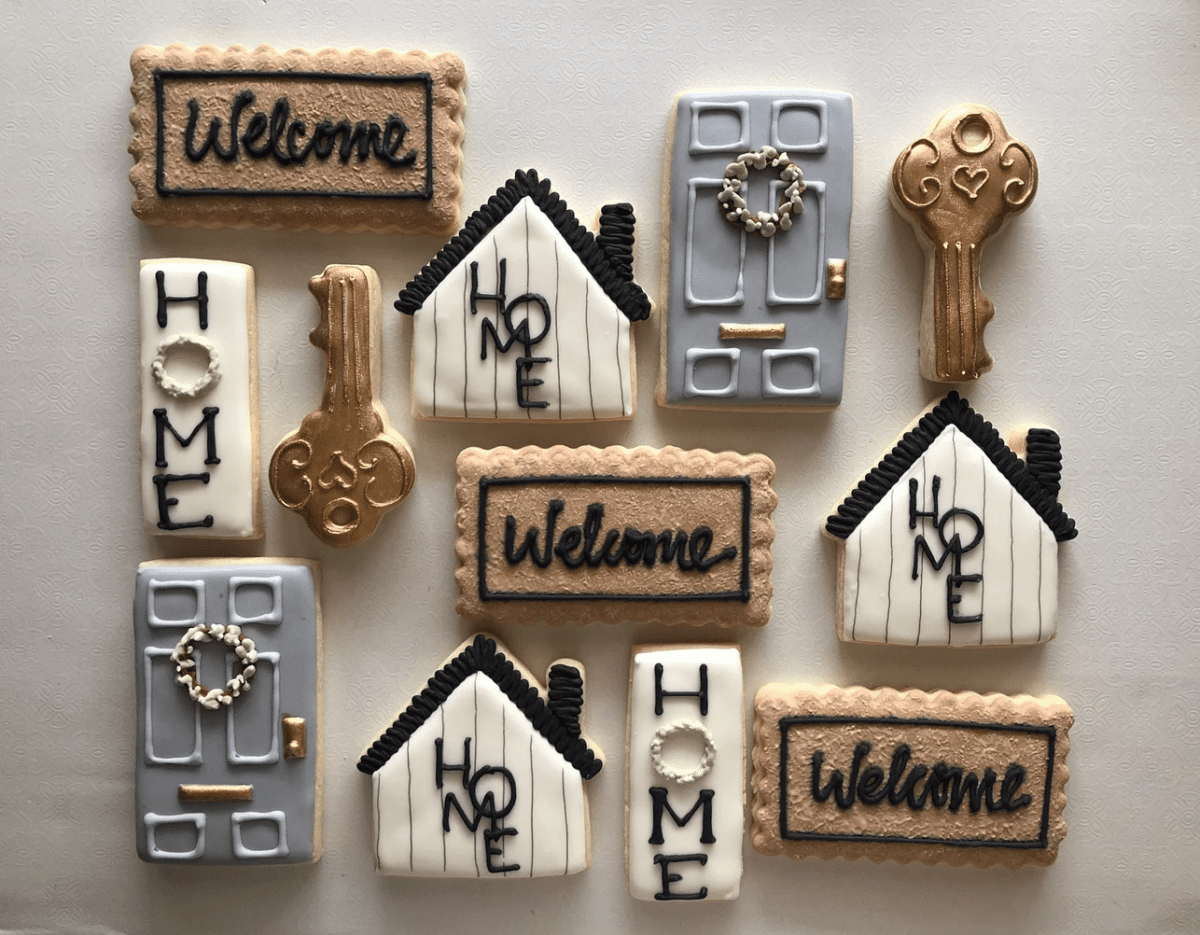 An assortment of cookies decorated as keys, doors, and houses, including the words welcome and home written on some of them.