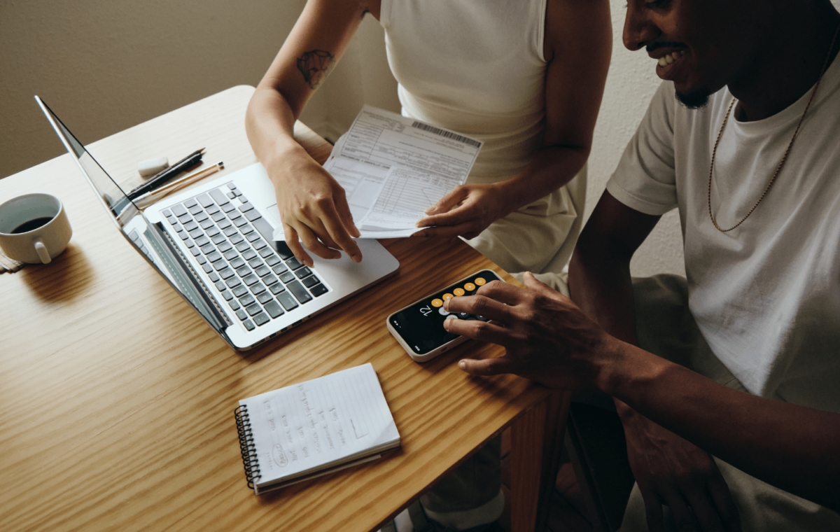 Couple sitting at a laptop looking at an invoice and using their phone as a calculator.