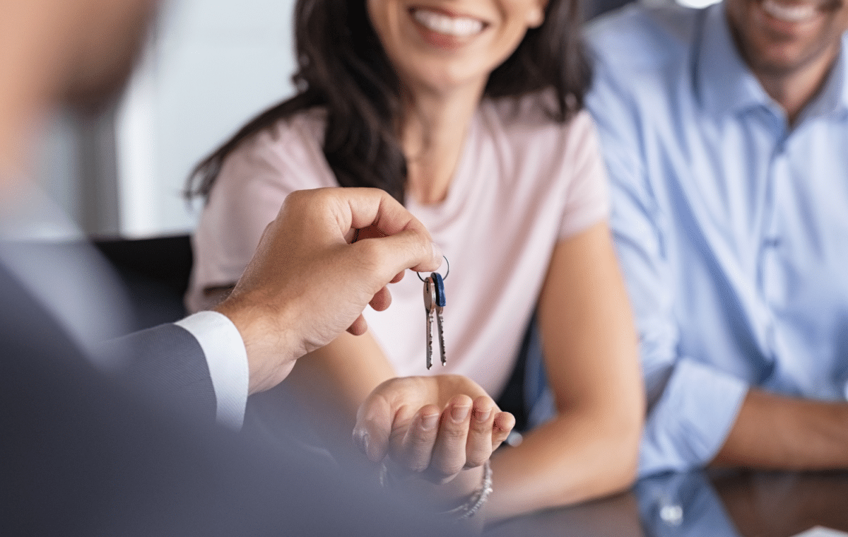  A man is handing a set of keys to a smiling woman who is holding out her hand.