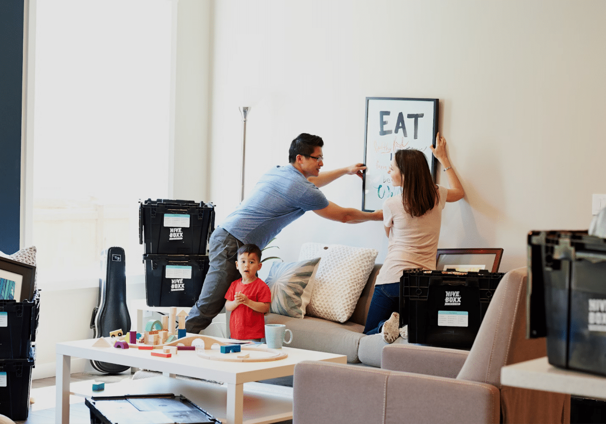 A family of three moving into a new apartment; a couple hanging a frame on the wall