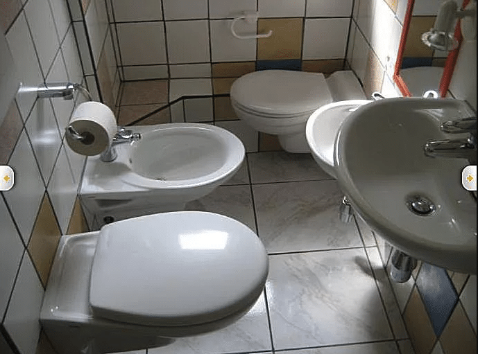 Tiled bathroom with two toilets on opposite walls, a bidet, and two sinks at different heights.