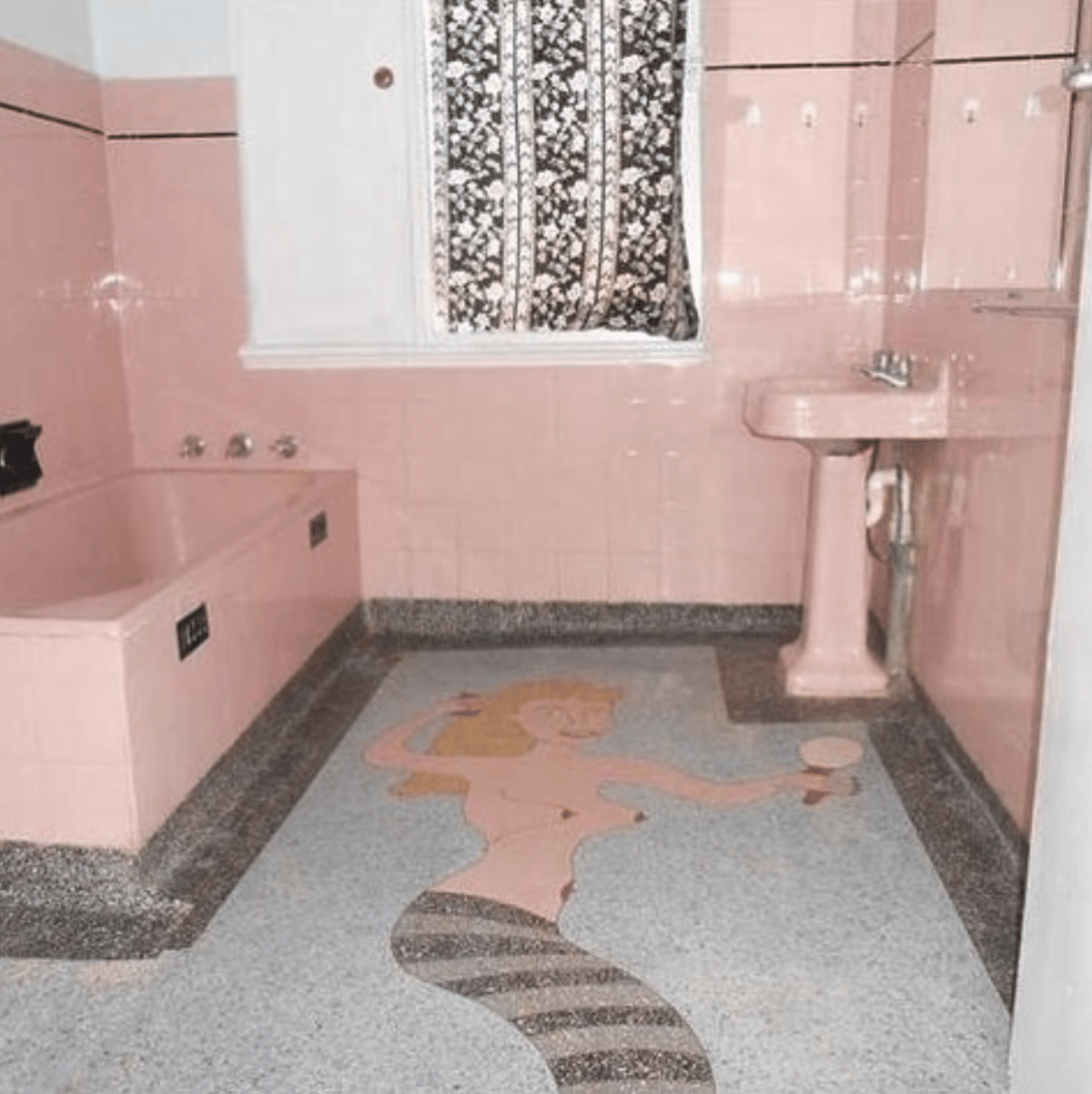 Tiled bathroom with pink tiles up the wall with matching pink sink and tub. The floor is a tiled mosaic of a mermaid holding a mirror and combing her hair.