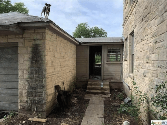 Entryway to a brick home with a small dog standing on the roof looking at the photographer.