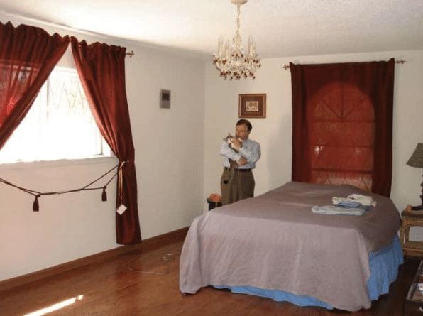 Bedroom with a bed and a man standing beside it holding a cat.