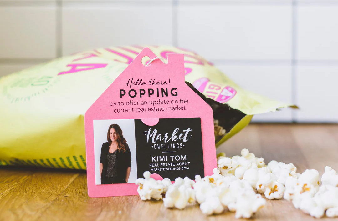 A real estate agent business card in front of a bag of popcorn lying on a table with popcorn spilling out of it.